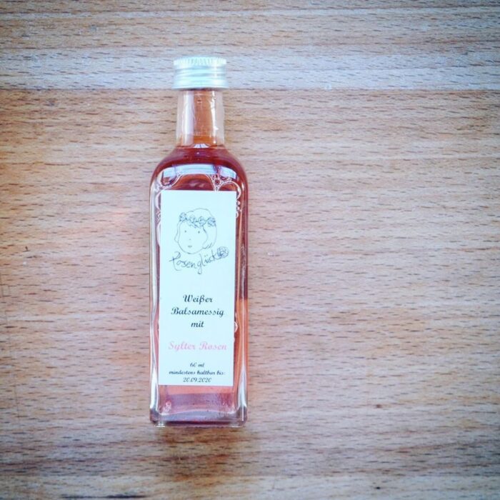 92515022_212054293388782_5489653651473604141_n Eine kleine Flasche SYLTER ROSEN BALSAMESSIG Öl auf einem Holztisch.