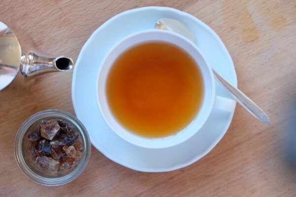 98F6D899-0152-45AD-87BE-DE5FE28501BD-2296-0000017C256CF2E5 Eine Tasse Tee auf einem Tisch neben einem Löffel und LUND SYLT - SYLTER RUMTOPF TEEMISCHUNG.