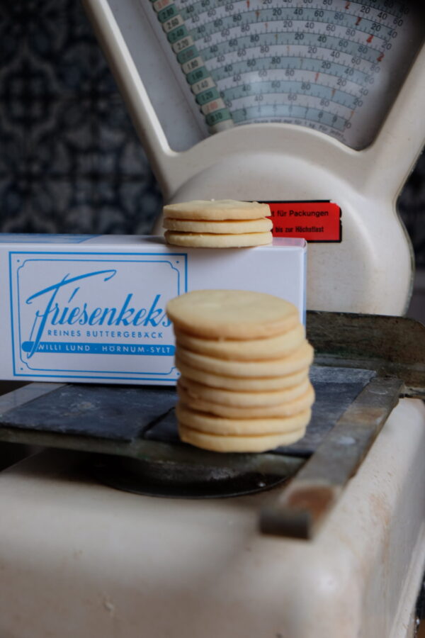 Ein Stapel FriesenKekse Ein Stapel FriesenKekse balanciert auf einer Vintage-Waage, im Hintergrund steht eine Schachtel mit der Aufschrift „FRIESENKEKSE 240 g“.