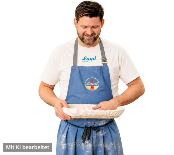 Jens Lund mit Lund Workwear natural raw-freigestellt – KI Ein Mann in einer blauen Schürze und dem Lund-Shirt – mit blauem Logo – hält eine abgedeckte runde Auflaufform in der Hand, lächelt und blickt darauf hinunter (Bild mit KI bearbeitet)