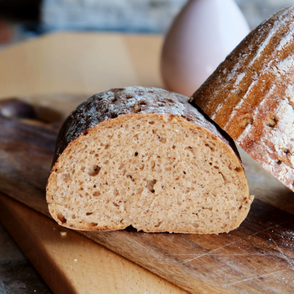 Lund Sylt Bio Roggenmisch 70-30 Roggensauerteig anschnitt Zwei Scheiben Landbrot auf einem Holzbrett, leicht mit Mehl bestäubt.