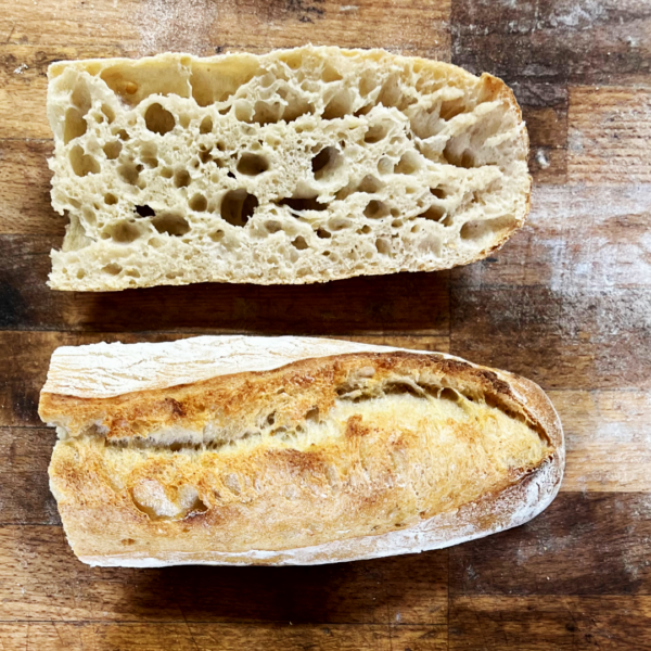 Lund Sylt Bio dinkelbaguette cut Auf einer Holzoberfläche aufgeschnittenes BIO-Dinkel-Baguette, das seine knusprige Außenseite und sein luftiges Inneres offenbart.