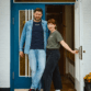 Jens Lund und Julia von Lund Sylt stehen vor einer blauen Holztür und tragen das LUND SHIRT mit weißem „Lund Sylt“-Logo, er in Navy unter einer offenen Jeansjacke, sie in Aloe (Bild mit KI bearbeitet)