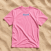 Pinkfarbenes LundSylt T-Shirt in XXL mit "Lund SYLT" in blauer Schrift auf sandfarbenem Hintergrund.