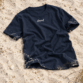 Sylt T-Shirt von Lund Sylt in Navy (French Navy) mit weißem „Lund Sylt“-Logo auf der Brust, locker auf hellem Sylter Strandsand mit Strandhafer liegend (Bild mit KI erstellt)