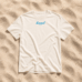 Ein weißes „LundSylt“-T-Shirt in Größe XXL mit auffälliger blauer Aufschrift liegt im strahlenden Sonnenlicht auf strukturiertem Sand (Bild mit KI erstellt)