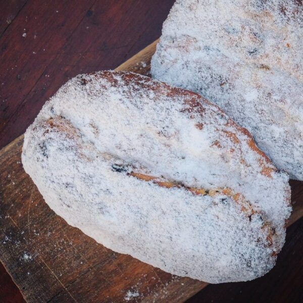 Sylter-stollen-Sylter-Milch-lund-sylt-online-shop Zwei Laibe SYLTER BUTTERSTOLLEN mit Puderzucker auf einem Holzbrett.