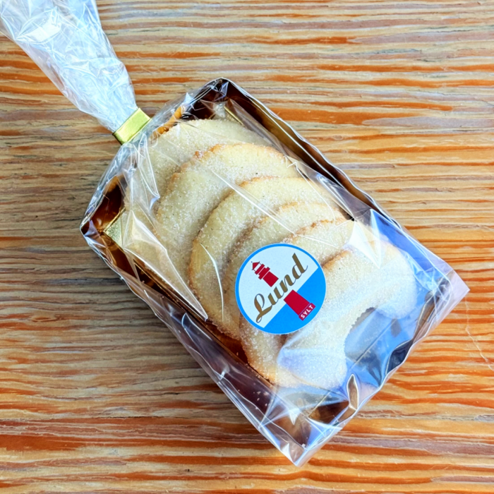 Tahiti Vanille Kipferl Kipfel Lund Sylt Eine Packung ringförmiger Kekse in Zuckerguss und transparenter Verpackung auf einer Holzoberfläche.