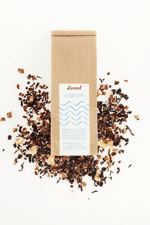 Tee-Rumtopf Eine Packung LUND SYLT – SYLTER RUMTOPF TEEMISCHUNG liegt inmitten einer herrlichen Mischung aus losen Teeblättern und Fruchtstücken und verkörpert die perfekte Mischung für ein reichhaltiges und aromatisches Gebräu.