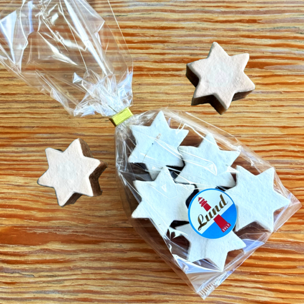 Zimtsterne Lund Sylt packung Sternförmige Kekse in einer durchsichtigen Tüte mit Lund-Etikett, auf einer Holzoberfläche platziert.