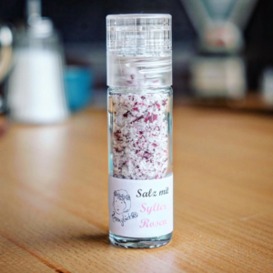 Die SYLTER ROSENSALZ MÜHLE präsentiert sich in einer eleganten Glasflasche mit einer fein gearbeiteten Mühle, gefüllt mit reinem Salz, gemischt mit zarten rosa Rosenblättern.