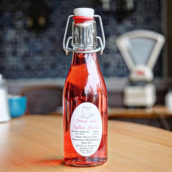 sylter-rosen-sirup-lund-sylt Eine Flasche SYLTER ROSENIRUP steht auf einem Holztisch.