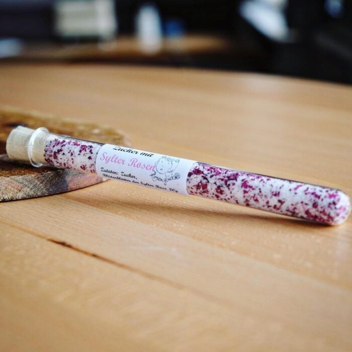 sylter-rosen-zucker Eine kleine Tube SYLTER ROSENZUCKER liegt auf einem Holztisch.