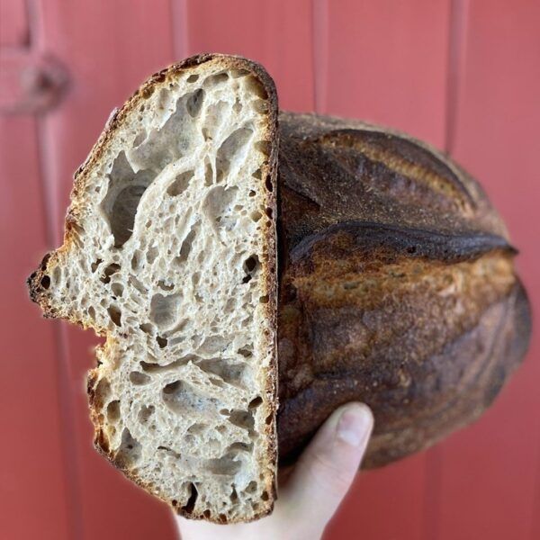 sylter_sauerteigbrot_Lund_Sylt-Quadrat Eine Person hält einen Laib Sauerteigbrot mit einem Loch darin hoch.